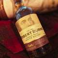 Bouteille de Single Malt Scotch Whisky Arran Robert Burns posée sur une étoffe de Harris Tweed®