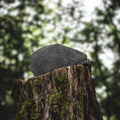 Casquette Baker Boy Harris Tweed® grise à motif chevrons posée sur une souche d'arbre moussue en pleine forêt.