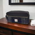Grande trousse de toilette Harris Tweed® au motif tartan gris et bleu marine posée sur un meuble en bois clair à côté d'une serviette de bain pliée.