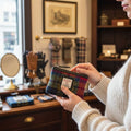 Gros plan d'une femme tenant dans ses mains le petit porte-monnaie Harris Tweed® au motif tartan multicolore bleu, vert, rouge, rose et violet dans une boutique de vêtements.