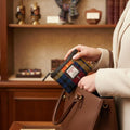 Gros plan d'une femme sortant de son sac à main le petit porte-monnaie Harris Tweed® au tartan jaune, bleu et rouge dans un décor de boutique élégante.
