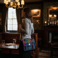 Femme de dos portant la petite sacoche Harris Tweed® tartan rouge, bleu et vert en bandoulière dans un pub.