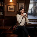 Femme dégustant un café dans un pub avec sa petite sacoche Harris Tweed® jaune, bleue et rouge portée en travers du corps.