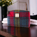 Petite trousse de toilette Harris Tweed® au tartan multicolore bleu, vert, rouge, rose et violet posée à côté de serviettes blanches moelleuses sur un plan de toilette sombre.