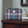 Petite trousse de toilette Harris Tweed® tartan aux nuances boréales (bleu, vert et violet) posée sur un meuble de salle de bain rustique.