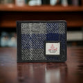Vue rapprochée du portefeuille 3 volets Harris Tweed® fermé, mettant en relief le tissage en tartan de la laine grise et bleue avec l'étiquette d'authenticité Orb Mark.