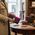 Femme tenant le portefeuille enveloppe Harris Tweed® aux couleurs vives (tartan rose, violet, bleu) devant un bureau en bois décoré.