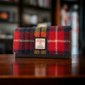 Portefeuille enveloppe Harris Tweed® posé sur une structure en bois vintage, mettant en avant la vivacité du tissage traditionnel écossais au motif tartan bleu, rouge et jaune.