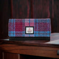 Portefeuille enveloppe Harris Tweed® posé sur un meuble en bois, mettant en avant le tartan bleu, rose et violet.