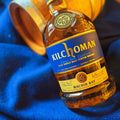 Bouteille de Single Malt Scotch Whisky Kilchoman Machir Bay posée sur une étoffe de Harris Tweed coloris bleu