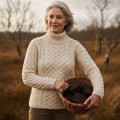 Femme portant le pull jumper en tricot de laine mérinos écru de style Aran dans la lande d'Irlande, tenant un panier de mottes de tourbe.