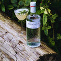 Bouteille de Gin Botanique London Dry The Botanist Islay Dry Gin posée sur un tronc d'arbre avec un verre de cocktail