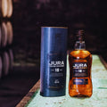 Bouteille de Single Malt Scotch Whisky Jura 18 ans et son étui posés dans un chai de whisky sombre