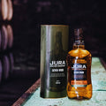 Bouteille de Single Malt Scotch Whisky Jura Seven Wood et son étui posés dans un chai de whisky sombre
