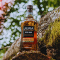 Bouteille de Single Malt Scotch Whisky Jura Seven Wood posée sur un tronc d'arbre dans la forêt