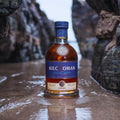 Bouteille de Single Malt Scotch Whisky Kilchoman Sanaig posée sur du sable mouillé dans une crique