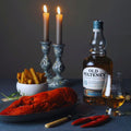 Bouteille de Single Malt Scotch Whisky Old Pulteney 15 ans posée sur une table à dîner avec des bougies, un homar et des frites